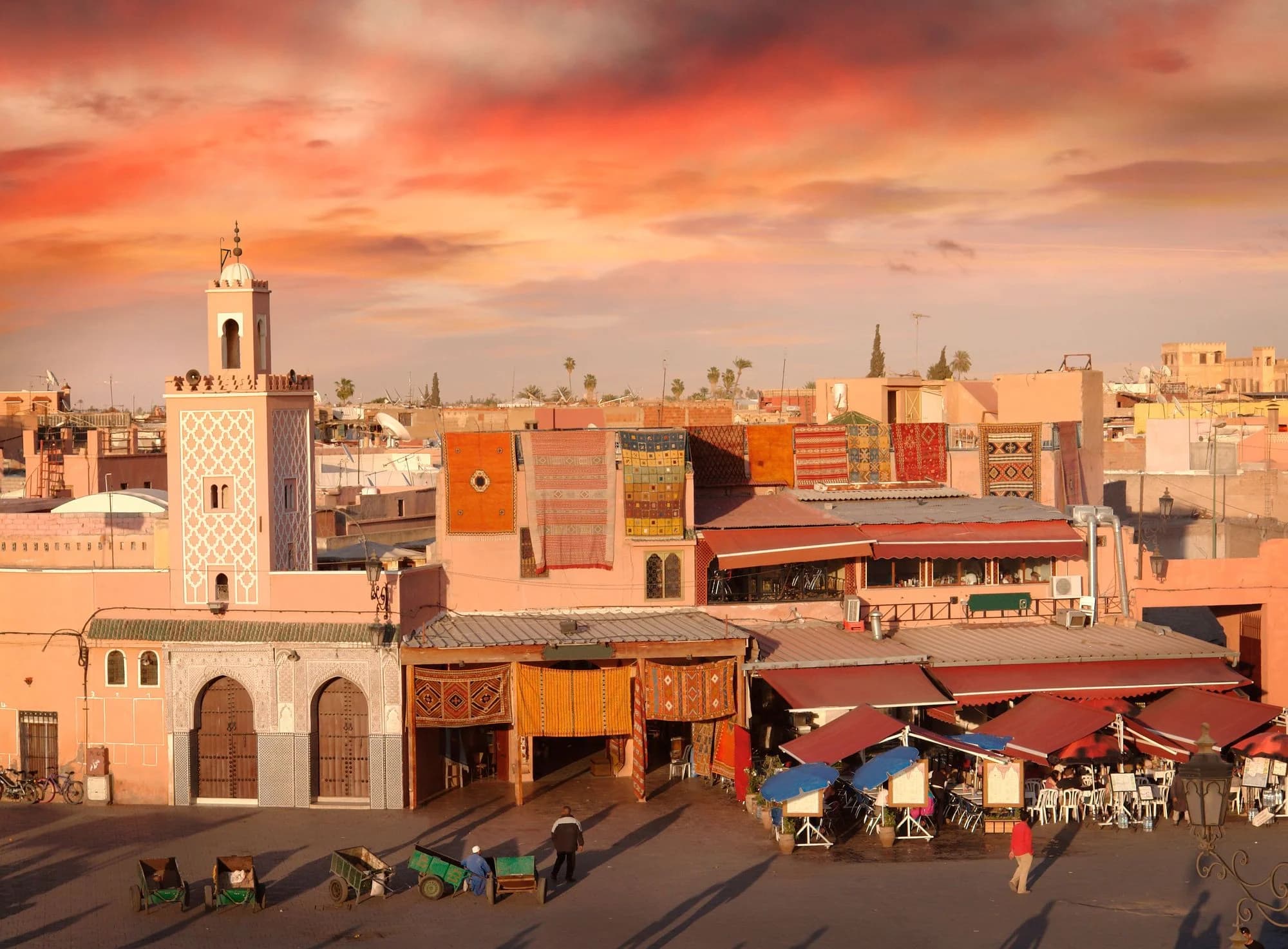 Pedestrians and motorbikes moving along a narrow terra-cotta alley in the Marrakech medina